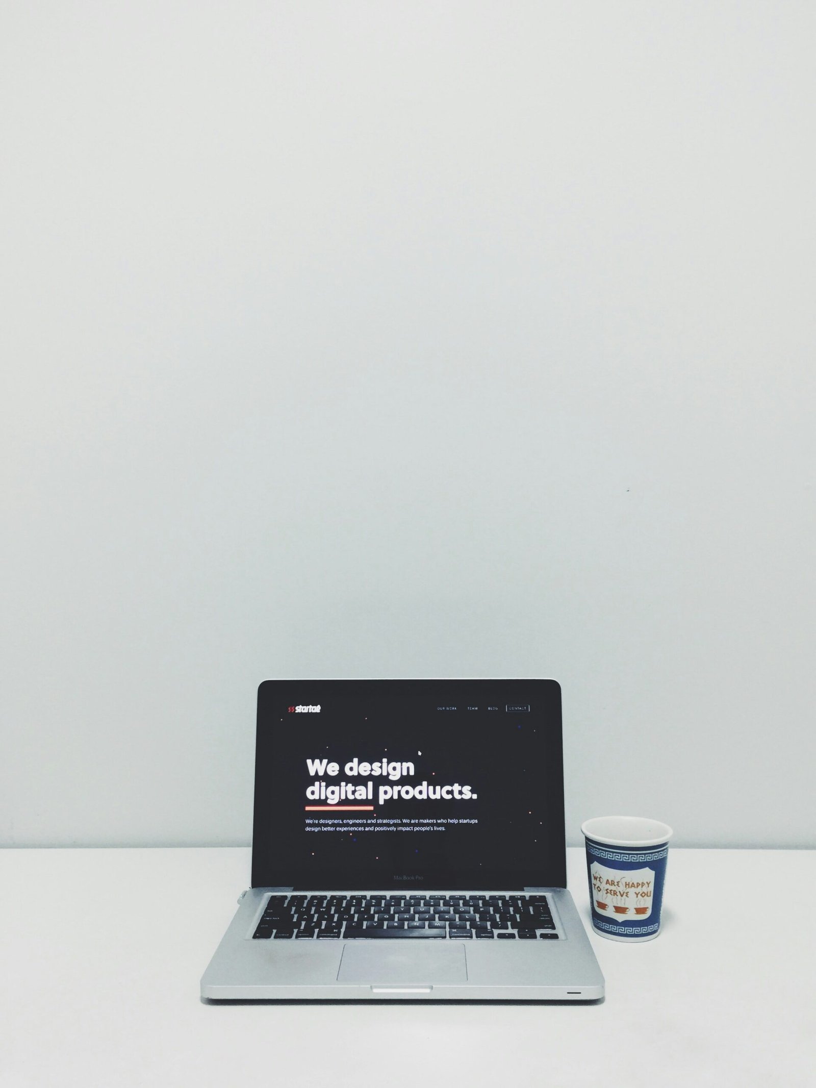 macbook pro beside white and blue plastic cup